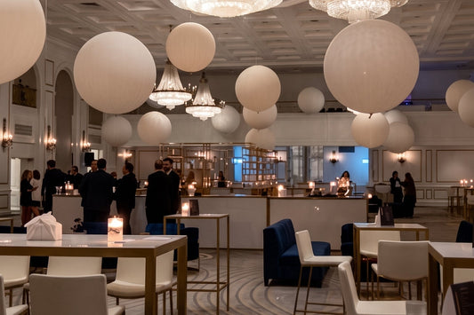 Fairmont Hotel in Toronto, multiple crystal chandeliers, large white cloudbuster floating balloons, patterned carpet, and dining tables with chairs. Several people are visible in the background near a bar or reception area