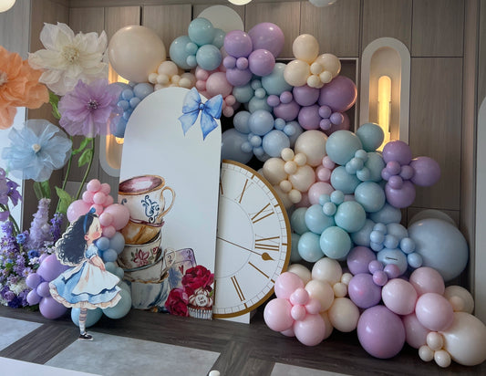 Alice in Wonderland themed balloon backdrop with pastel balloons, giant paper flowers, and whimsical tea party props.
