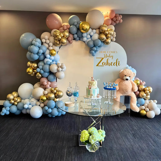 Elegant baby shower balloon garland in pastel blue, blush pink, and gold with custom arch signage and teddy bear setup