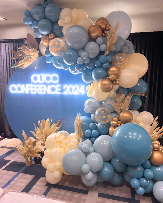 Luxury balloon backdrop in blue, gold, and ivory for corporate conference event with custom signage