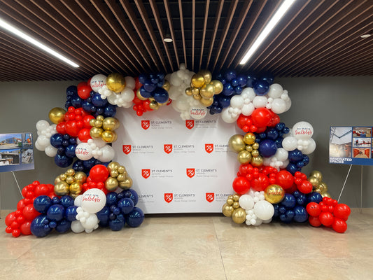 A luxury organic balloon arch in navy, red, and gold, professionally framing a custom step and repeat backdrop for a St Clement's school graduation and corporate event in Toronto by WeBalloonz.