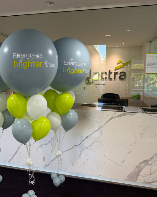 Branded helium balloon bouquet in gray, lime green, and white with "Energize a brighter future" logo, ideal for conferences, launches, and corporate parties.