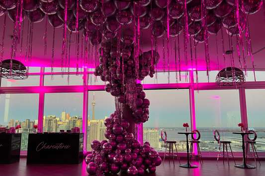 Luxe pink and purple metallic balloon installation in a high-rise venue overlooking the Toronto skyline and CN Tower at sunset.