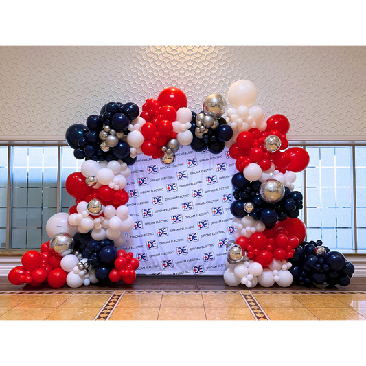 Custom red, white, and navy organic balloon arch framing a corporate step and repeat backdrop installation by WeBalloonz.