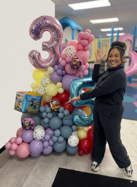 Colorful stand-alone balloon garland for a Paw Patrol-themed birthday party, featuring large number balloons for ages 3 and 5, pastel and primary colors, and themed foil balloons with a smiling woman posing beside the display.
