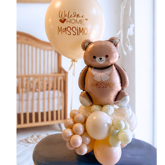 Personalized Welcome Home baby balloon gift featuring a large teddy bear balloon, creamy balloon cluster base, and jumbo balloon with custom vinyl text "Welcome Home Massimo.