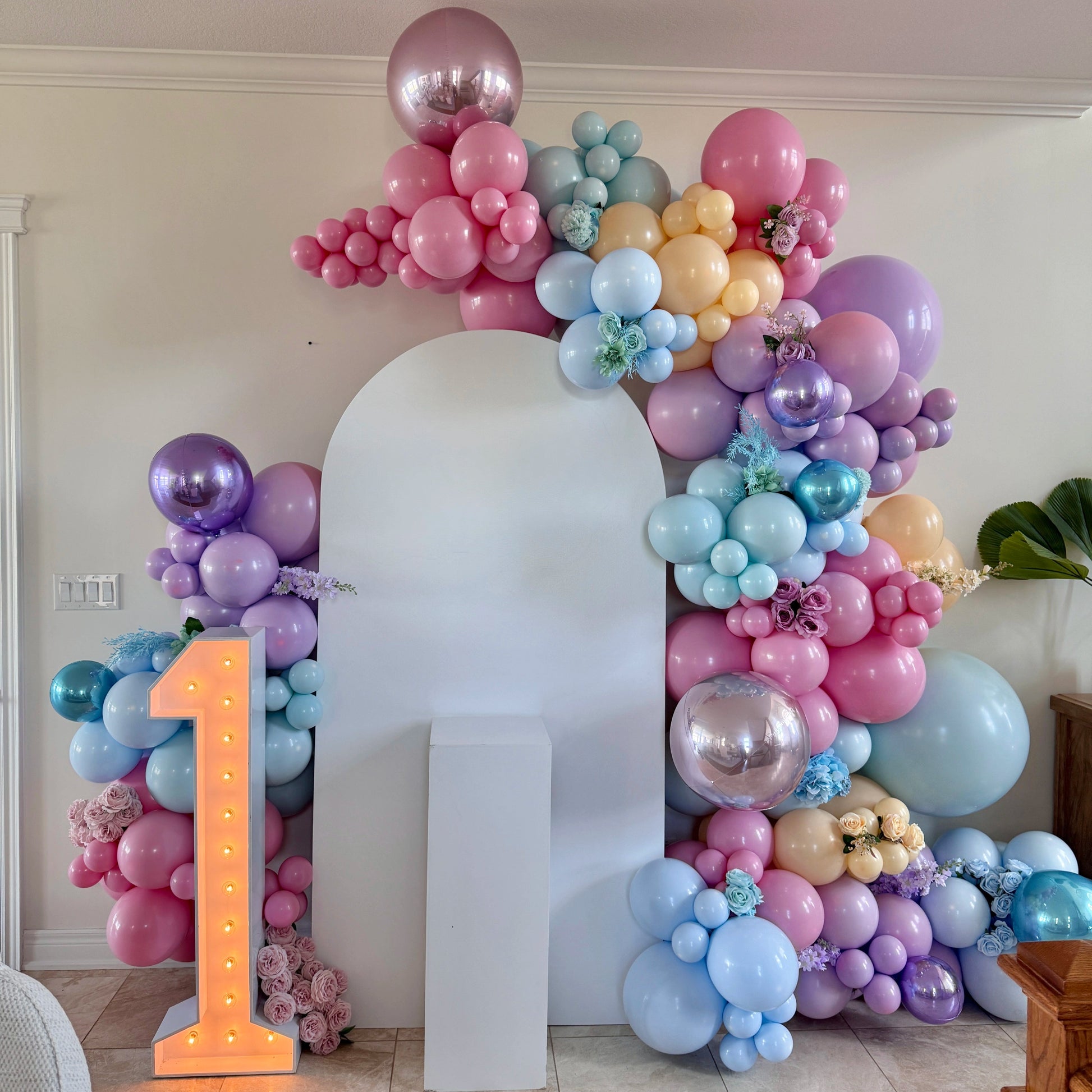 Colorful pastel balloon garland with number one marquee and white arch backdrop for first birthday party decoration