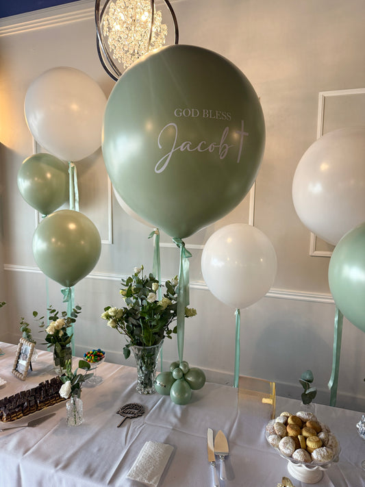 Large sage green custom "God Bless Jacob" helium balloon with white and green balloon bouquet and fresh floral centerpieces for a high-end baptism in Vaughan by WeBalloonz.