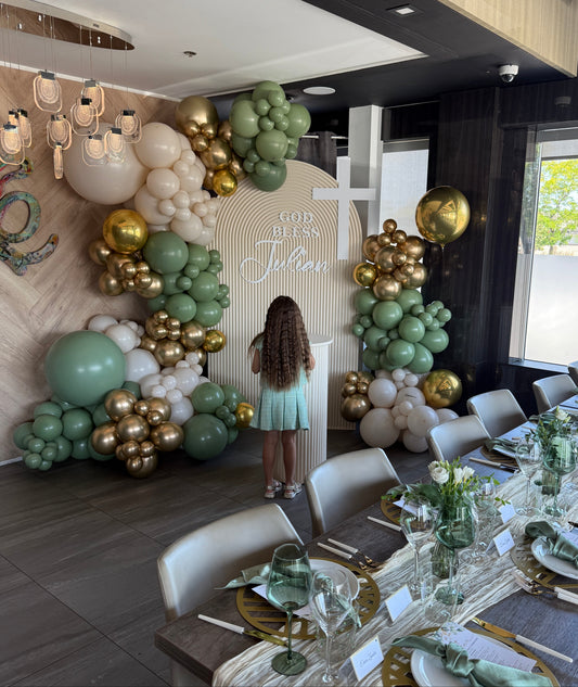 Sage green, gold, and cream organic balloon install with a custom "God Bless Julian" arched backdrop and cross for a luxury communion in Vaughan by WeBalloonz.