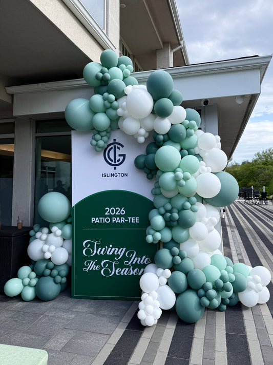 A large balloon garland arrangement in shades of mint green, teal, and white decorates the entrance to a building. A central sign reads '2026 PATIO PAR-TEE Swing Into The Season' with a visible Islington Golf Club logo above it.