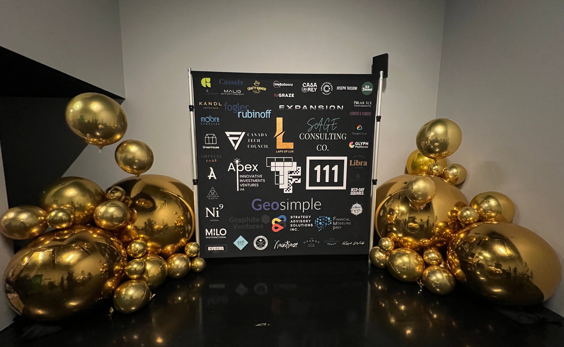 Corporate event balloon backdrop with gold chrome balloons and branded sponsor signage