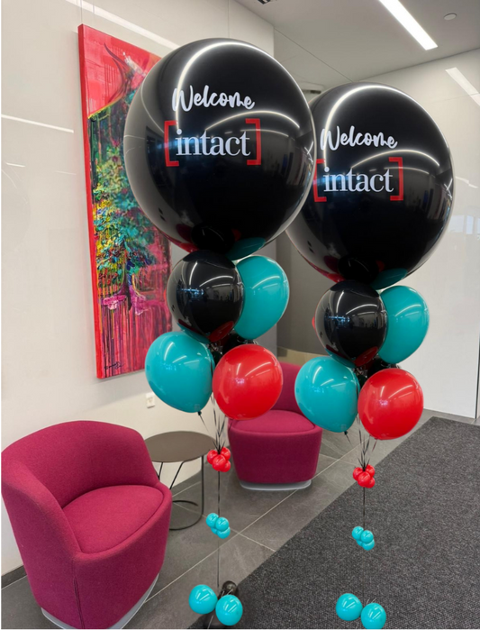 Custom helium balloon bouquet with black, teal, and red balloons featuring Intact logo branding for corporate welcome events and office celebrations.
