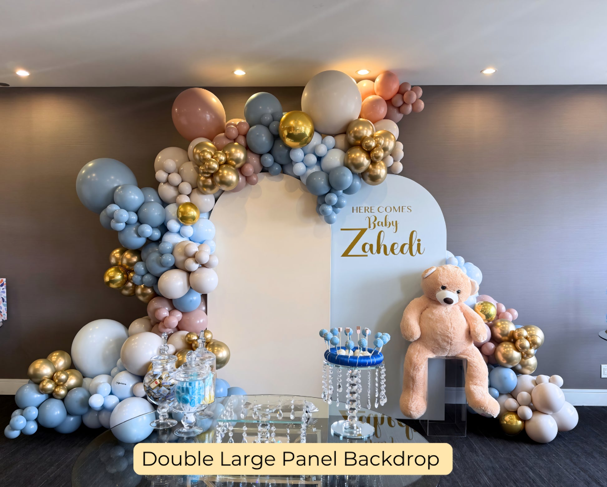 Double large panel balloon backdrop in blue, blush, and gold for baby shower with teddy bear and crystal dessert table display.