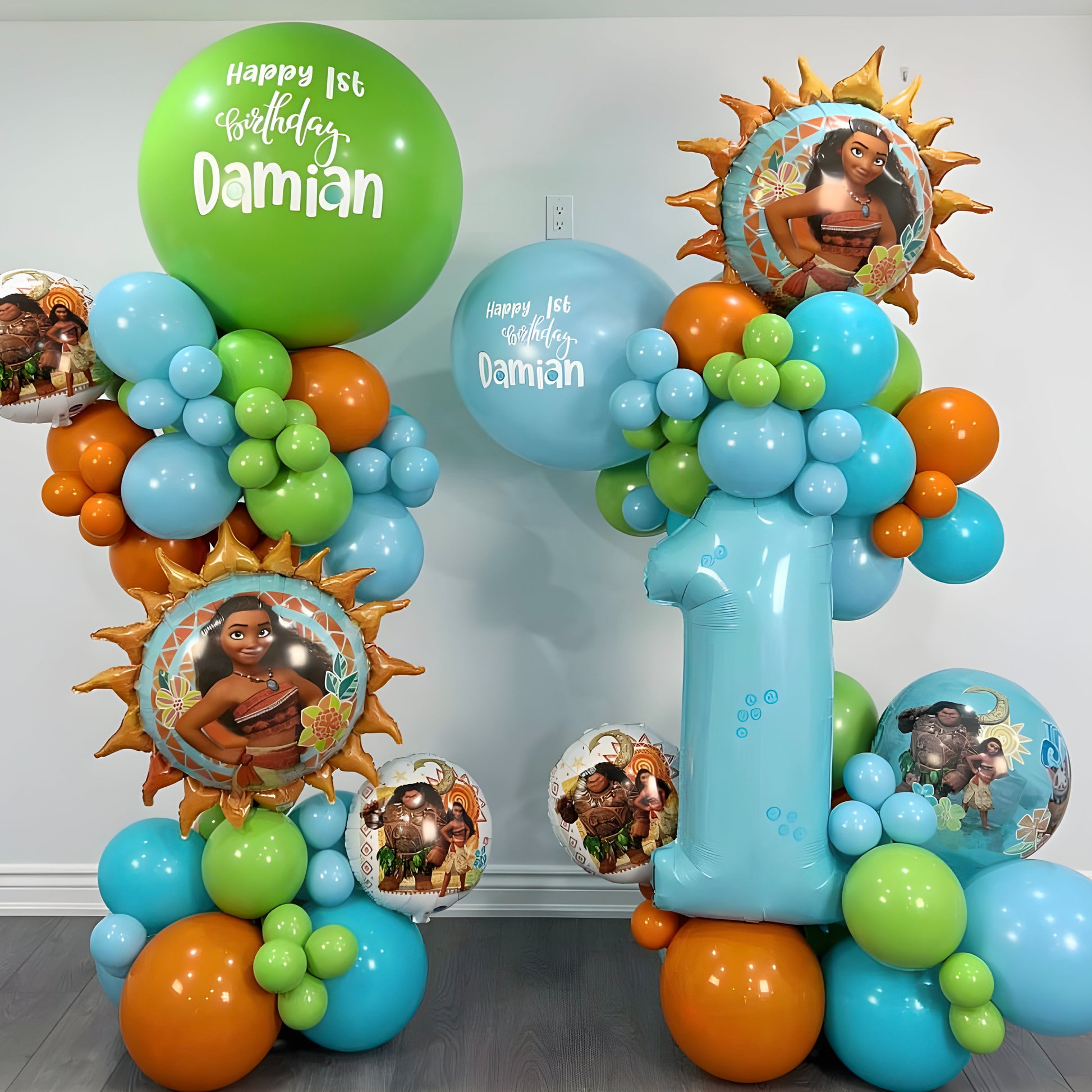 First birthday balloon tower with Moana theme, giant number 1 balloon, personalized jumbo balloon, and colorful organic balloons in blue, green, and orange