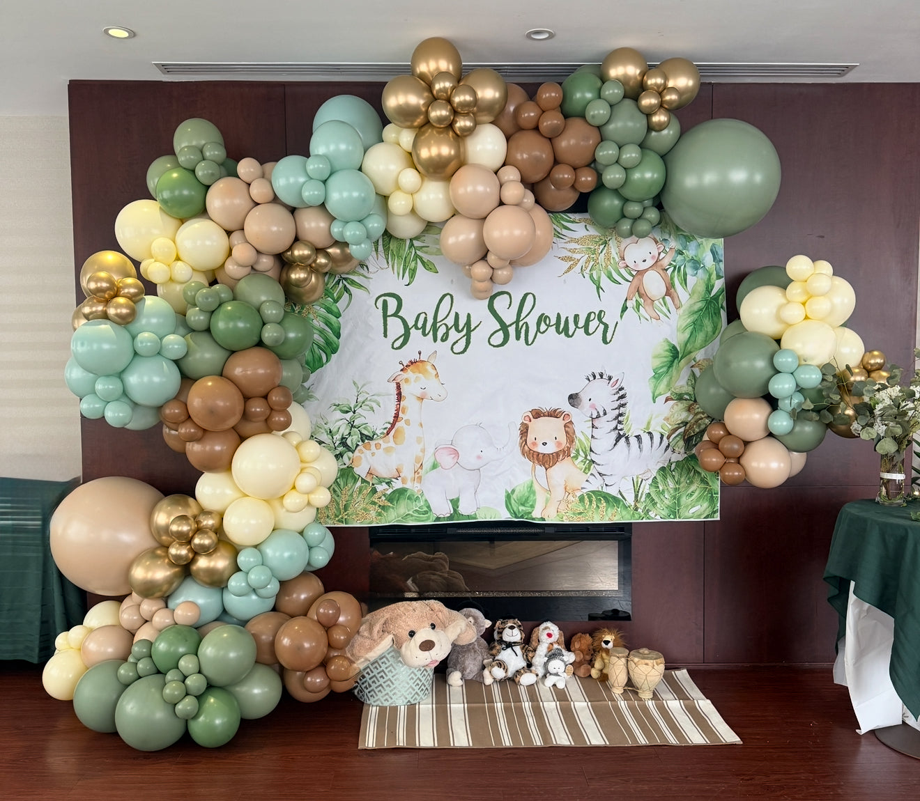 Luxury jungle-themed balloon garland with earthy tones for a baby shower, featuring safari animals and plush toys.