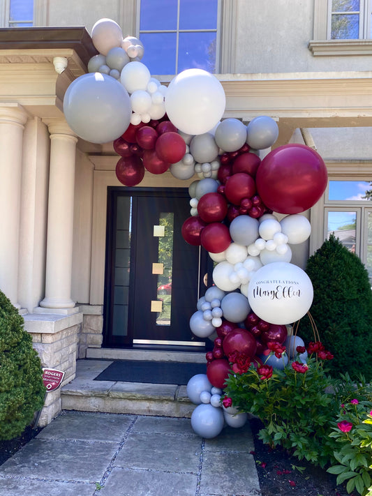 A bespoke 18ft burgundy, grey, and white organic graduation balloon garland custom-framed around a modern home entrance in Vaughan, featuring a personalized jumbo focal balloon by WeBalloonz.
