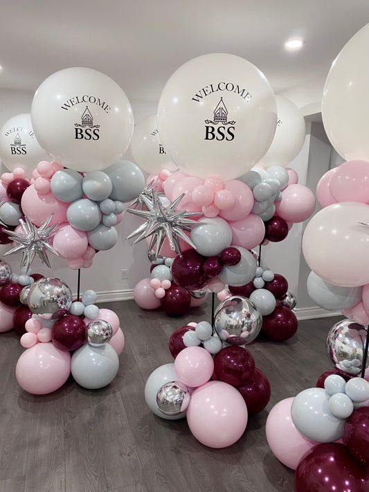 Bespoke 7ft graduation balloon towers in a soft pink, burgundy, and grey palette, featuring jumbo focal balloons with custom 'Welcome BSS' school branding in Toronto by WeBalloonz."