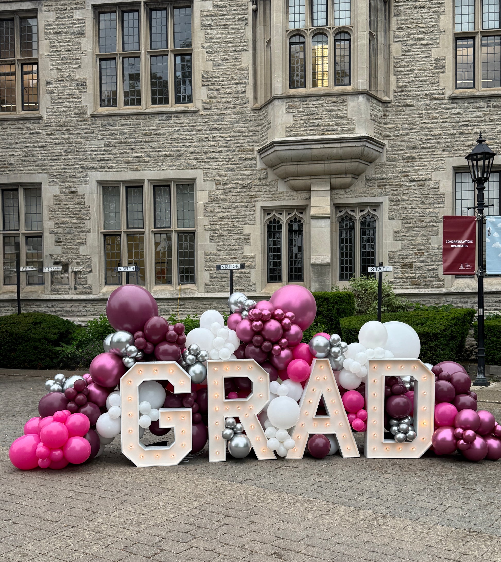 A grand 14ft wide graduation display featuring 3ft tall illuminated GRAD marquee letters surrounded by a custom organic balloon installation in Toronto by WeBalloonz.