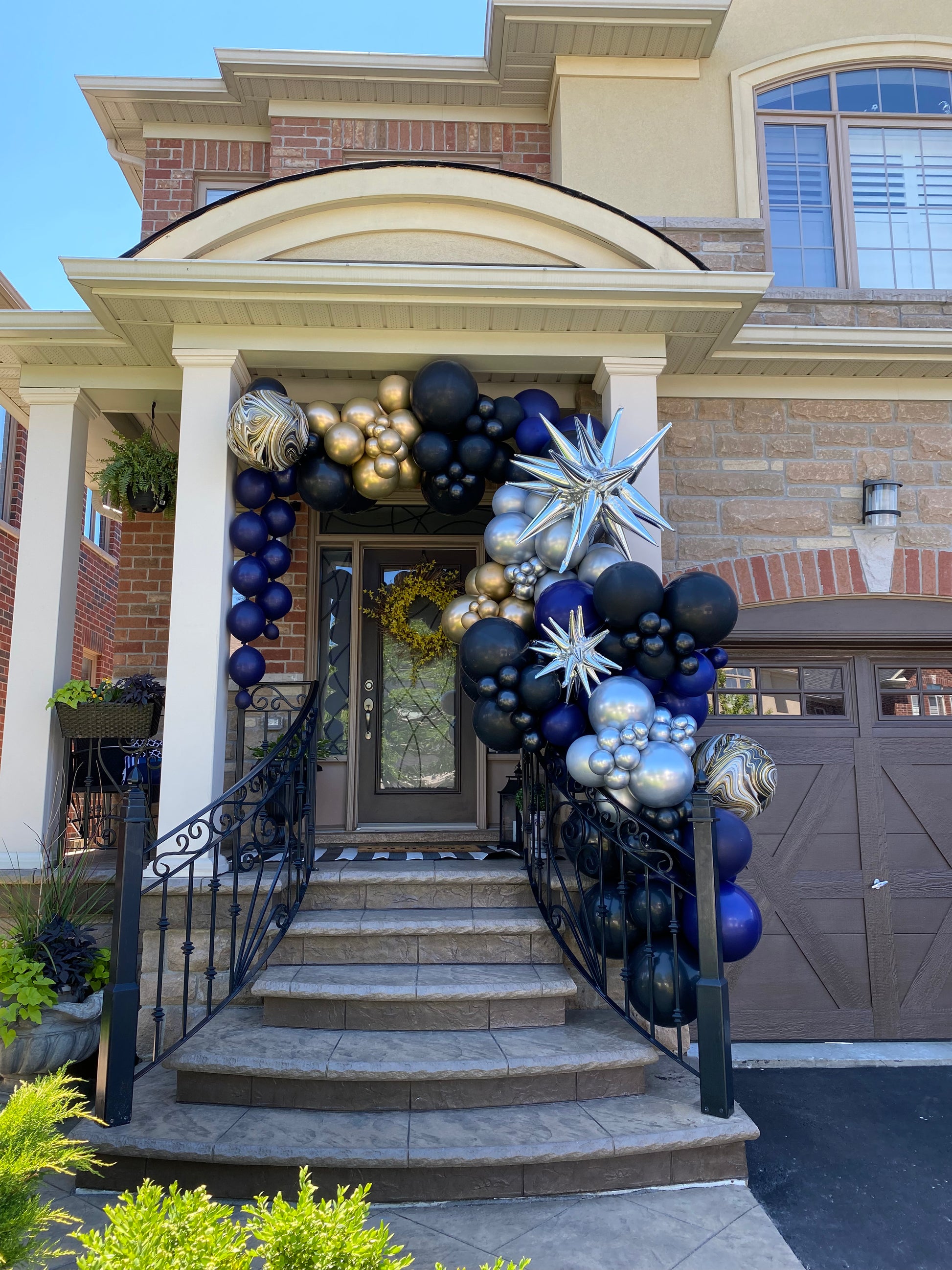 A grand 18ft luxury organic balloon installation in navy, black, and gold with silver starburst accents, custom-designed to frame a residential porch for a prom celebration in Vaughan by WeBalloonz.