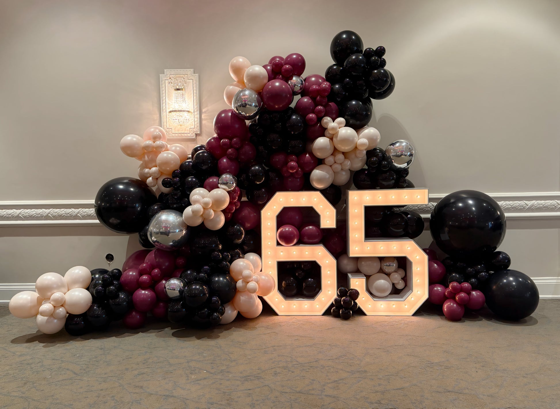 Elegant 65 marquee numbers with black, burgundy, blush, and chrome balloon garland for a stylish milestone celebration.