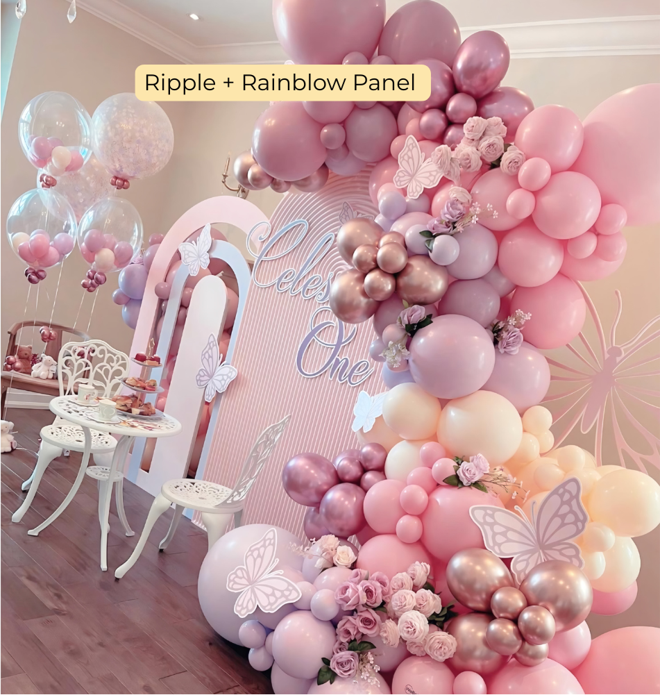 Dreamy pastel pink balloon garland with ripple and rainbow backdrop, butterflies, and floral accents, perfect for a whimsical first birthday or baby girl celebration