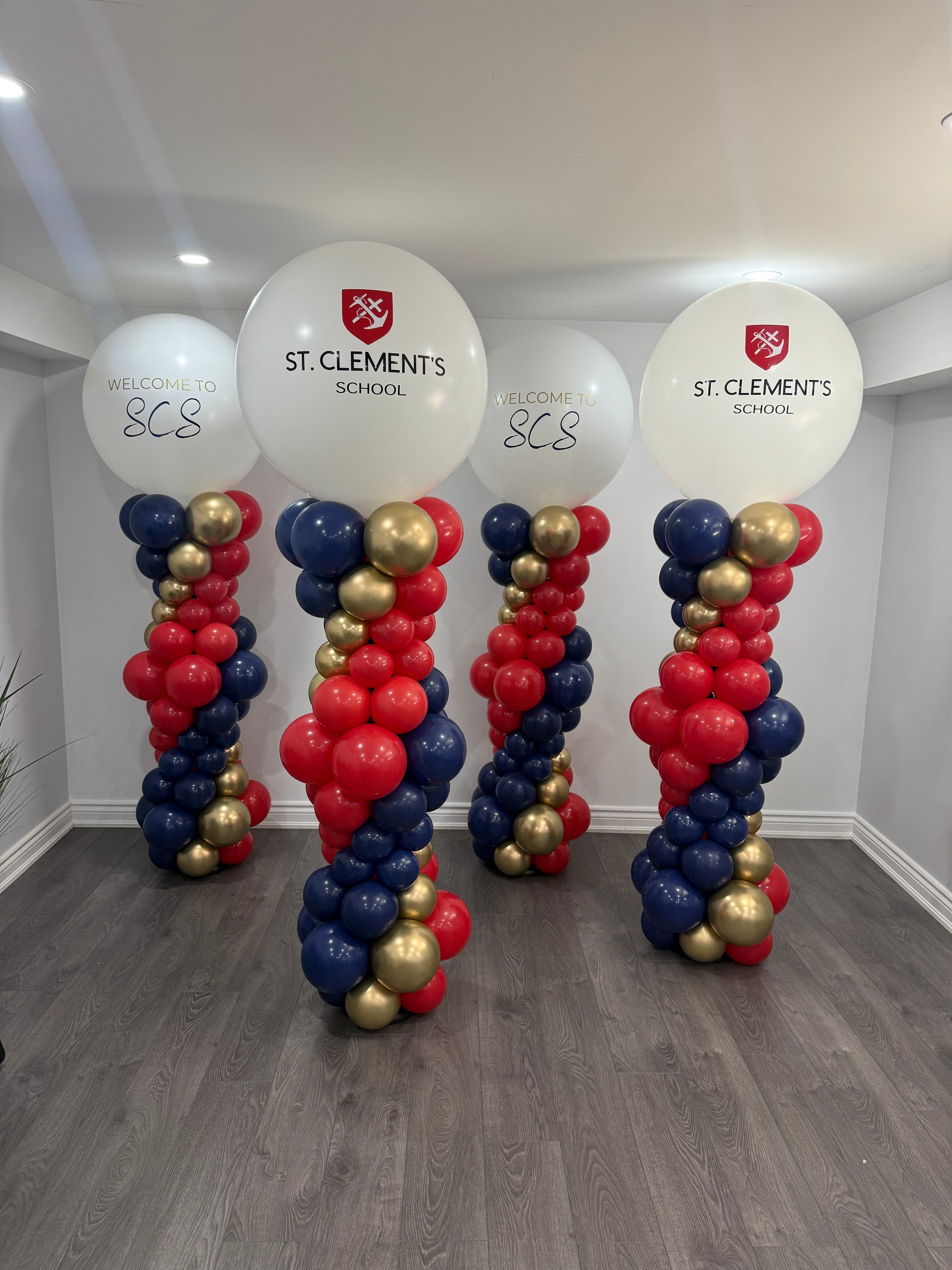 Four professional 7ft tall graduation balloon towers in navy, red, and gold, featuring the St. Clement's School logo and 'Welcome to SCS' messaging on jumbo focal balloons by WeBalloonz