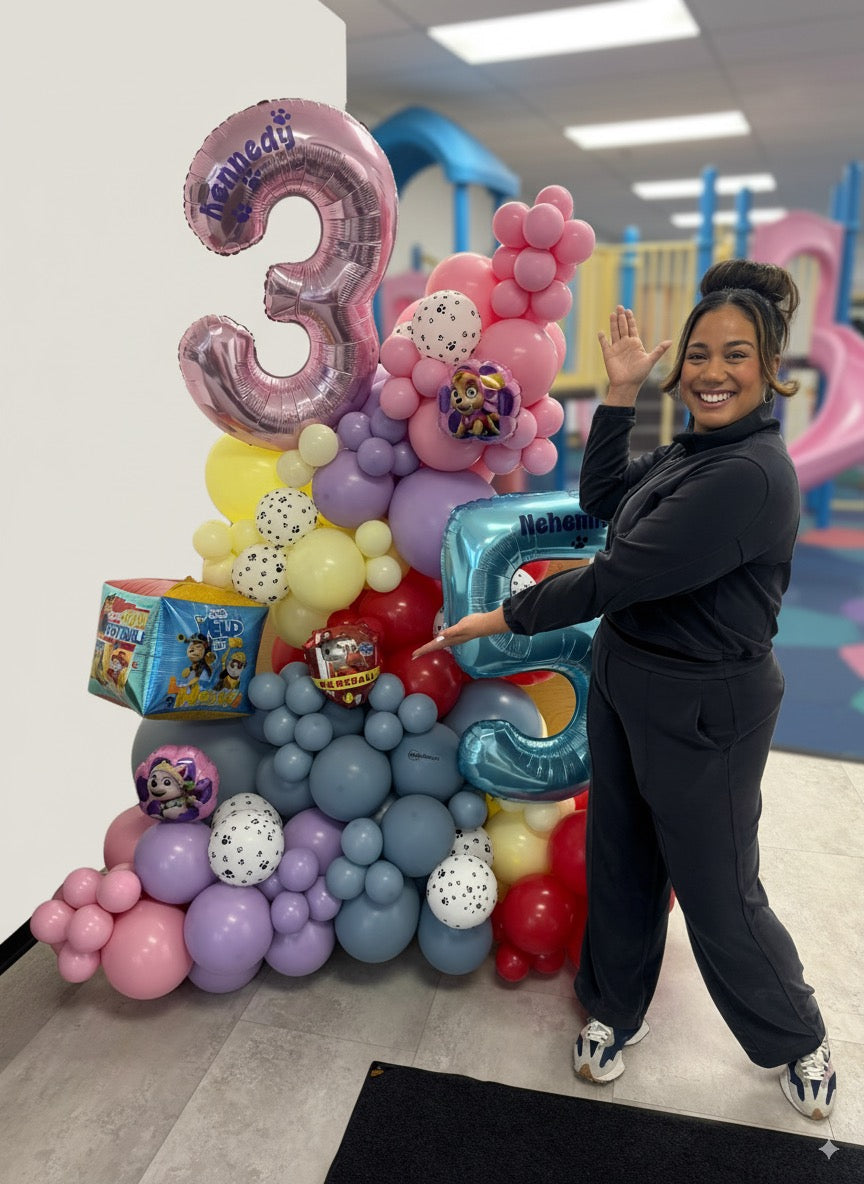 Colorful stand-alone balloon garland for a Paw Patrol-themed birthday party, featuring large number balloons for ages 3 and 5, pastel and primary colors, and themed foil balloons with a smiling woman posing beside the display.