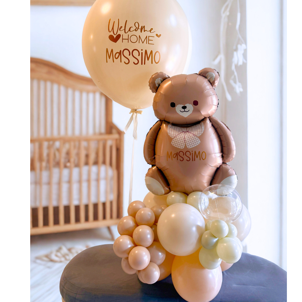 Personalized Welcome Home baby balloon gift featuring a large teddy bear balloon, creamy balloon cluster base, and jumbo balloon with custom vinyl text "Welcome Home Massimo.