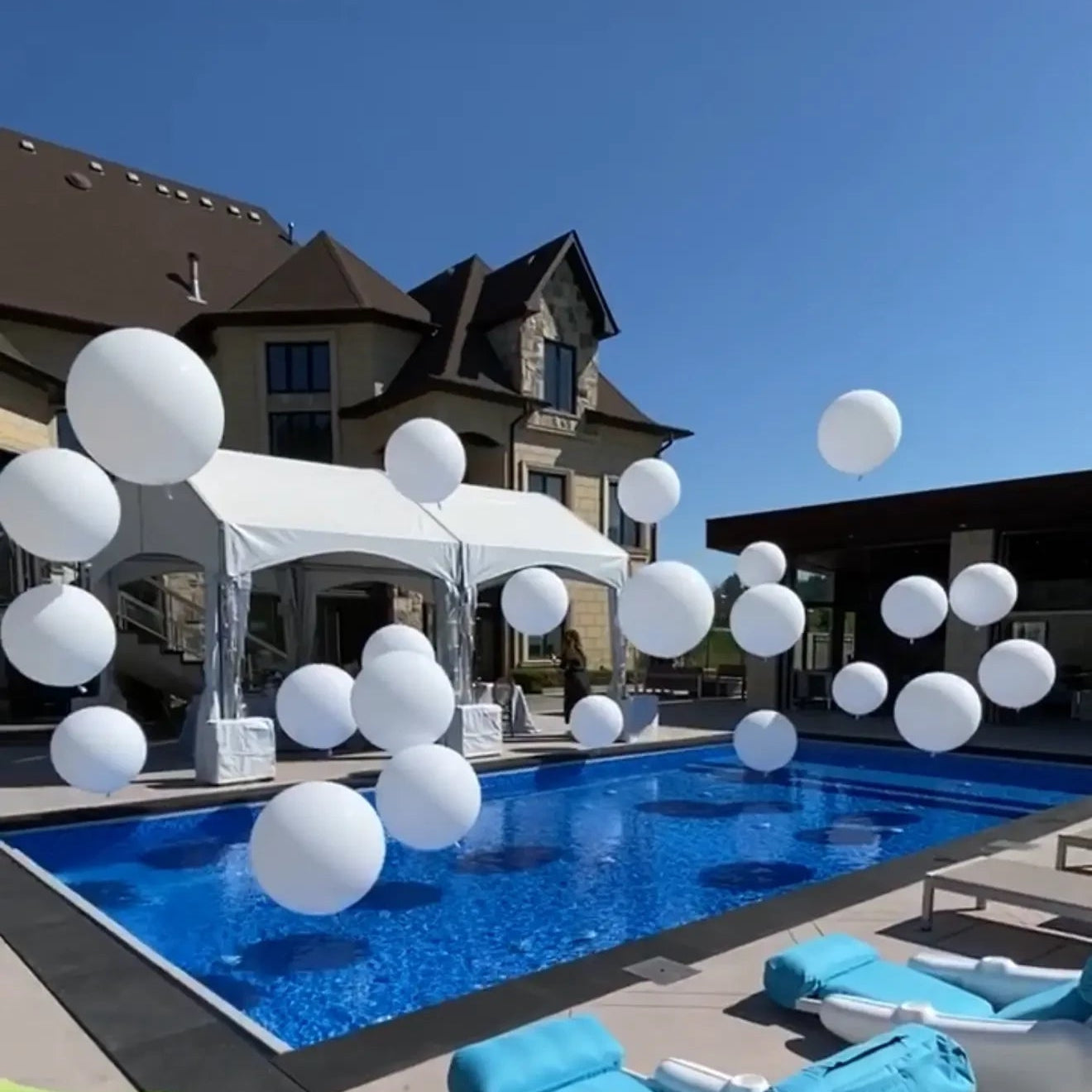 Large white balloons floating over a luxury backyard pool setup for a summer event in Toronto
