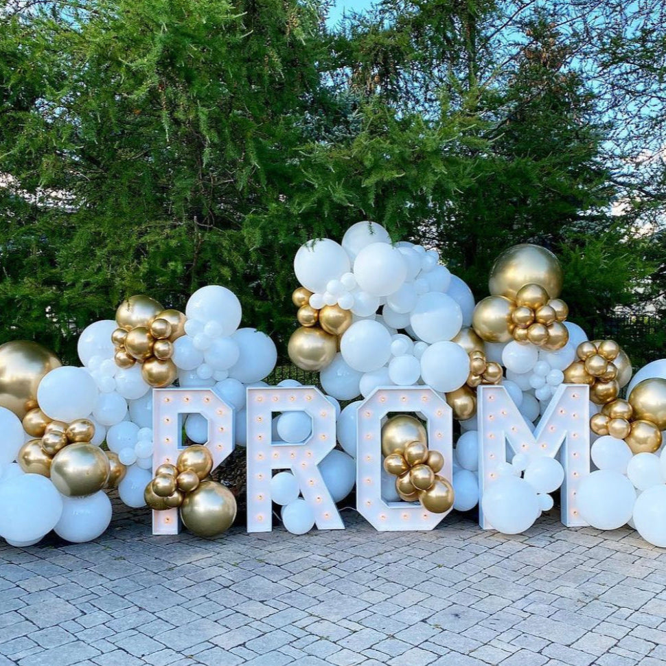 White and gold balloon garland with large marquee PROM letters — luxury outdoor prom backdrop setup for photo ops and event entrances.